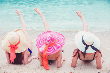 Sexy bikini body three asian women enjoy the sea by laying down on sand of beach wearing millinery hat.