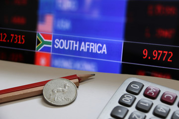 Coin of South Africa in reverse of a coin with deer form on wooden and red pencil with calculator on the white floor and digital board of currency exchange money background, the concept of finance.