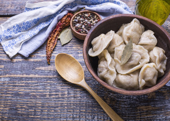 Homemade boiled dumplings of their dough and minced meat, olive oil, spices, salt, pepper, bay leaf on a wooden board, background.