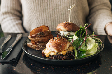 Delicious burgers with lettuce and fries on black plate in cafe