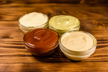 Different sauces in glass bowls on wooden table