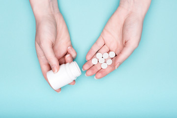 Close up of female hands holding medication bottle and white pills over pastel blue background....