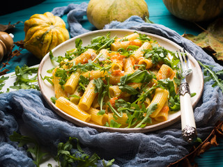 Pasta with baked pumpkin, arugula and onion. Rustic green autumn background with pumpkins and dry...