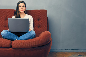 Girl with laptop sitting on red sofa.