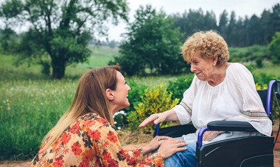 Affectionate young woman talking to elderly woman in a wheelchair in the garden
