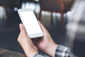 Mockup image of hands holding white mobile phone with blank screen on wooden table in cafe