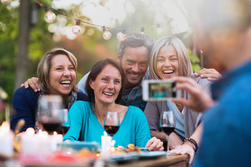 Obraz premium Some friends in their forties gathered around a table in the garden for a good time. A man takes a picture of a group of friends