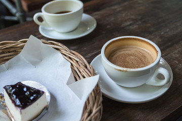 Closeup image of two coffee cups and a cake in basket on vintage wooden table in cafe