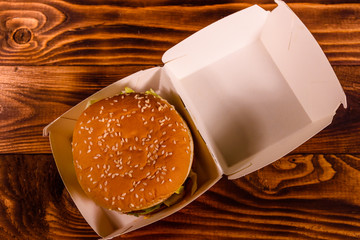 Fresh hamburger in paper box on the rustic wooden table. Top view