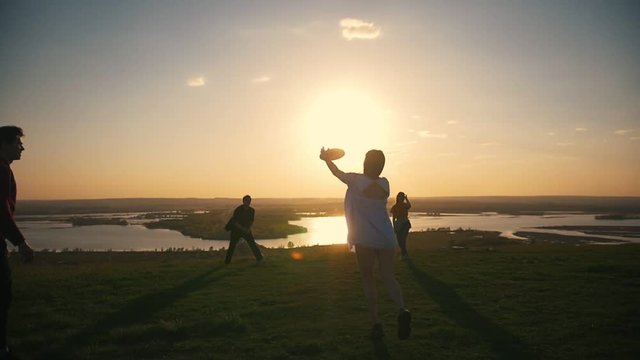 Happy young friends playing frisbee at summer sunset on the hill