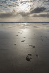 close up on footsteps on sandy ground in beautiful golden sunset on biscarrosse beach, france