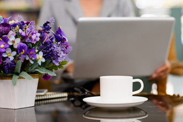 white cup of coffee with a notebook computer and glasses on a wooden desk.
