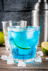 Colorful summer beverage, iced blue lagoon alcohol cocktail drink with lime and mint, bark background copy space