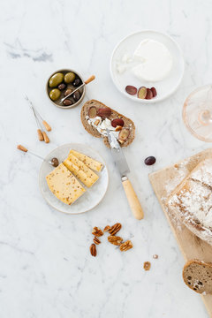 Cheese platter with bread, nuts, olives and grapes on a marble table.