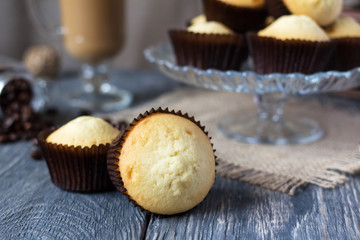 Lots of cakes in glass vase, in foreground two cupcakes in molds, on old table