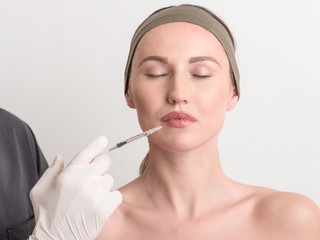Close up of hands of cosmetologist injecting botox in female face. The woman is closed her eyes with relaxation.