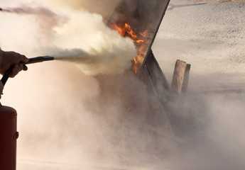 Fototapeta premium Man using powder type fire extinguisher fighting fire close up photo
