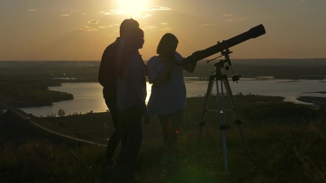 Young man showing friends beautiful view through telescope at summer sunset