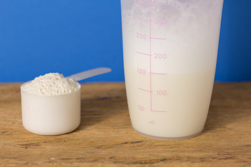 Whey Protein. Close up of scoop with vanilla powder and shaker over wood table. Color background: blue.
