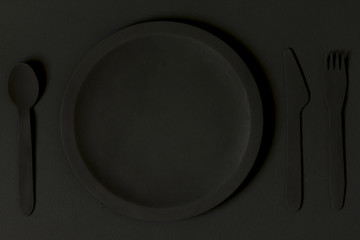 View of a round wooden plate with cutlery on a black board