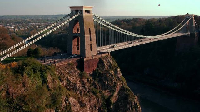 Camera pans across the Clifton Suspension Bridge during a beautiful sunset. A hot air ballon is in the sky