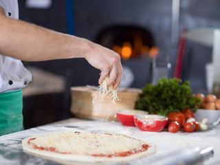 chef sprinkling cheese over fresh pizza dough