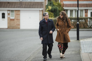 Mature couple are talking and laughing as they walk down the residential street together. 