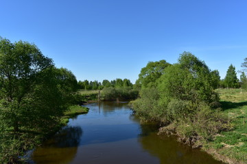 landscape flowing river, steep banks, green trees, blue sky