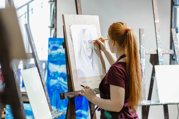 Red-haired girl paints a picture. Bright Art Studio with large Windows.