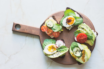 Different sandwiches with vegetables, eggs, avocado, tomato, rye bread on light marble table. Top vew. Appetizer for party. Flat lay.