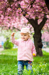 little charming blonde playing with pleasure in the garden with blooming cherry blossom