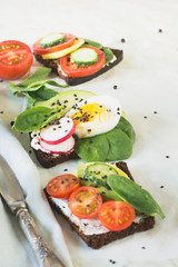 Summer sandwiches with vegetables, eggs, avocado, tomato, rye bread on light marble table. Appetizer for party. Close up.