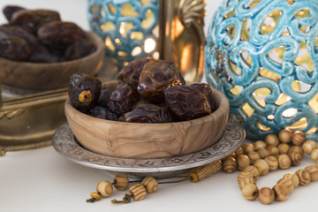 Date fruits and wooden rosary on the white background with blue candle for Muslims Ramadan and three months concept.