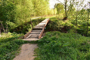 Fototapeta na wymiar landscape wooden bridge over stream, rusty metal handrails, background green trees, grass