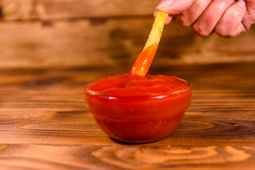 Hand with fresh french fry dipped into the tomato sauce