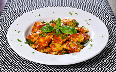 Fresh ravioli pasta with parsley and basil leaf, italian cuisine. White plate and wooden table, pasta dish.