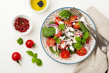Tomatoes, spinach leaves, red onions and feta cheese salad on a light ceramic plate. Selective focus. Top view.