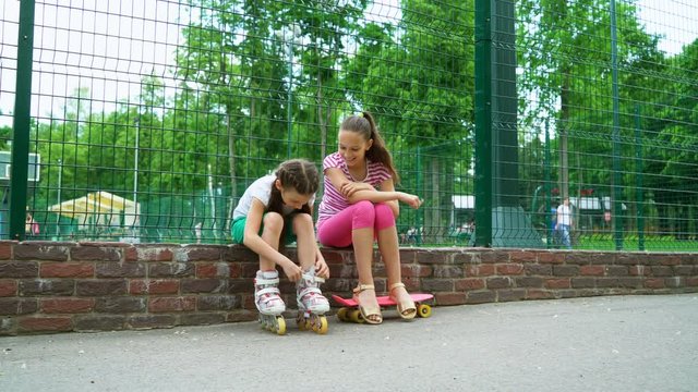 two girls active passtime in park. young teen dresses roller skates, sisters preparing skating. fun and joy leisure time.