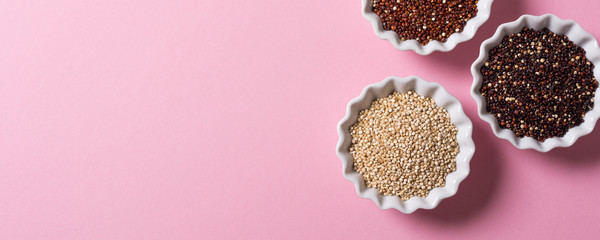 Flat lay of assorted Quinoa in white bowls on pink background. Overhead shoot with copy space. Healthy gluten free food concept. Banner.