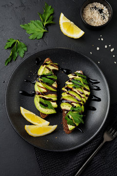 Spicy rye toasts with avocado, lemon and balsamic sauce on black concrete old background. Selective focus. Top view.