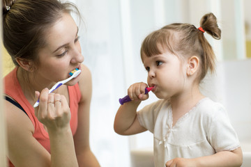 Mother and her daughter child brushing teeth together in the morning - dental care concept