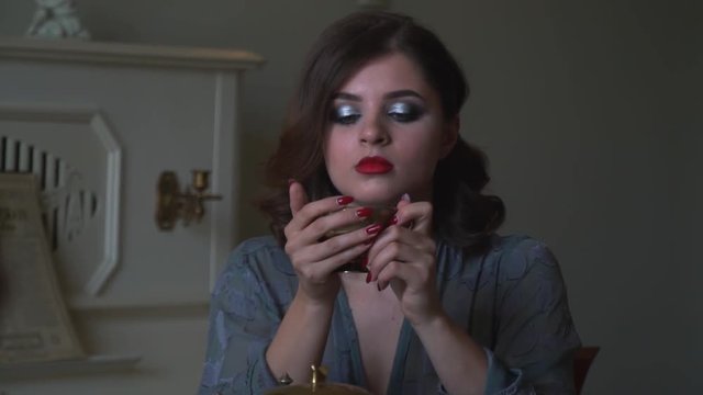 A girl with red lips is drinking tea from a golden cup