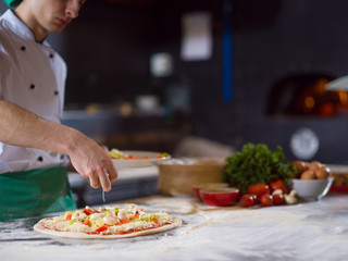 chef putting fresh vegetables on pizza dough