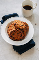 American chocolate chip cookies  in a white plate cup of coffee on a white stone background. Top view.