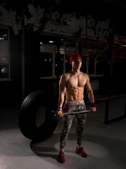 Fototapeta na wymiar A young sportsman in a red cap in the gym. Do exercises with a hammer. Crossfit training in the gym.
