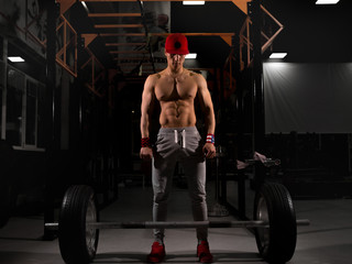 Obraz na płótnie Canvas A young sportsman in a red cap in the gym, raises the bar with wheels. Crossfit training in the gym.