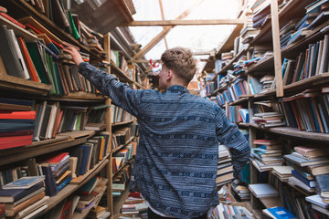 Back of a student walking around the old home library in search of books. Portrait of a man looking for books in a cozy, atmospheric library.