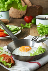 Fried egg in a frying pan with vegetables on a wooden table            