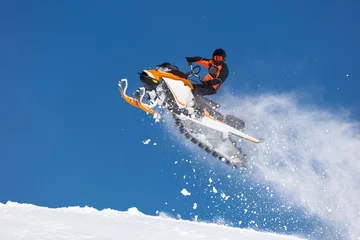 Fotobehang the guy is flying on a snowmobile on a background of blue sky leaving a trail of splashes of white snow. bright snowmobile and suit without brands. © Wlad Go