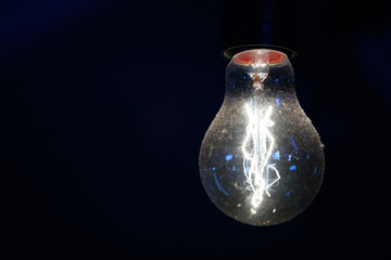 vintage glowing light bulb on dark background. on the surface of the glass dust. cool color, the location of the lamp on the right close-up